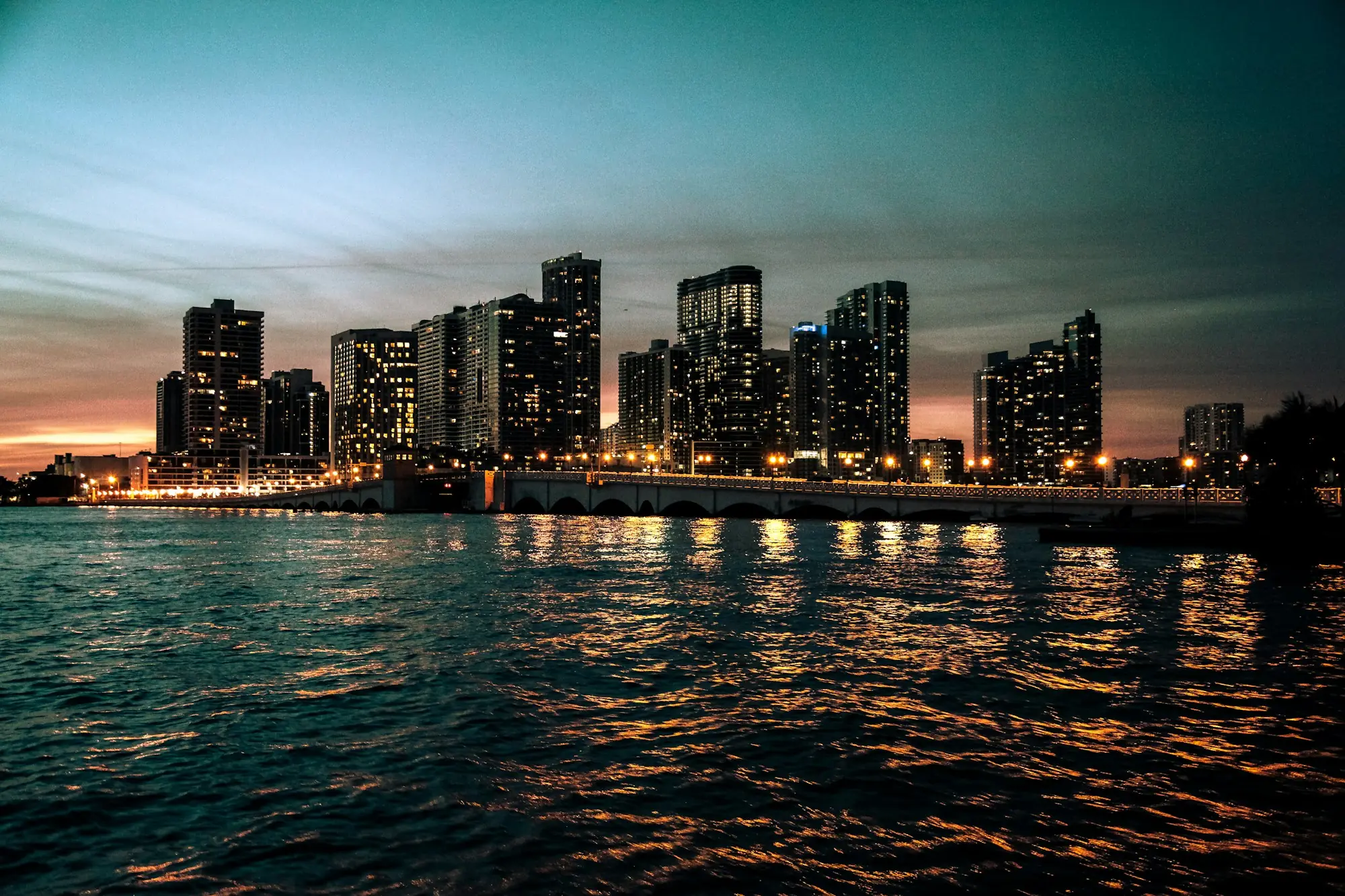 Residential towers on Biscayne Bay at dusk, their lights reflected in the water